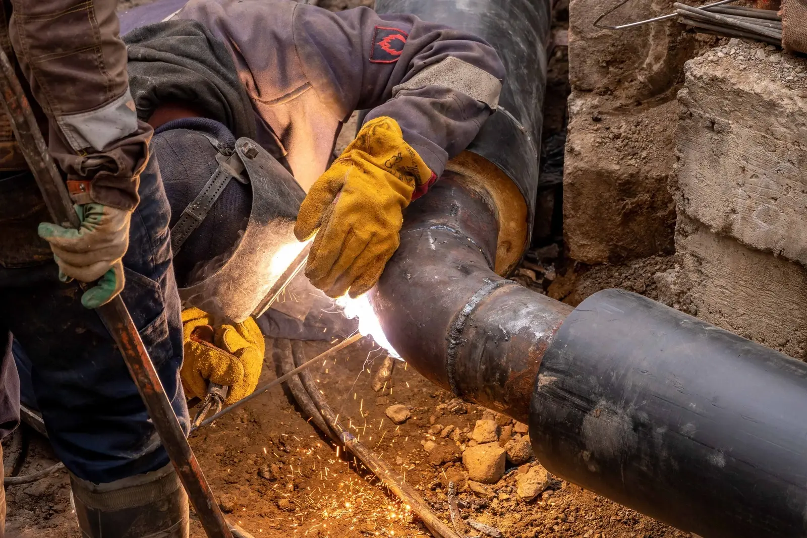 Illustrative image: a welder joining pipes on site, sparks flying